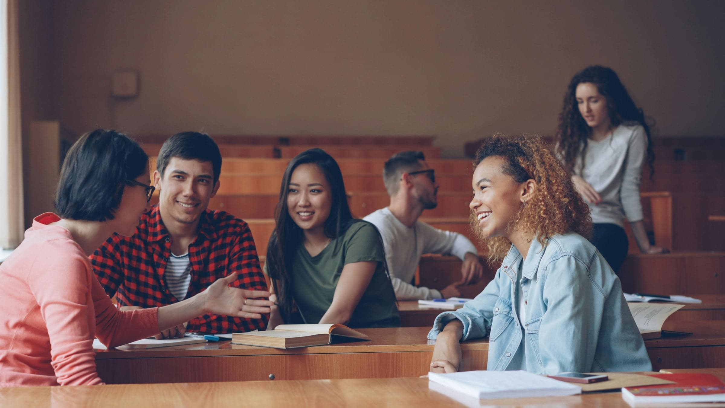 Students talking together around desks in a warm, wood-panelled lecture hall